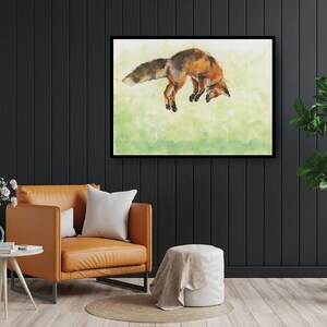 May include: A framed watercolor painting of a fox in shades of orange, brown, and white against a green background. The fox is depicted mid-leap, with its head down and tail extended. The artwork is displayed on a black wall.