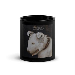 Könnte beinhalten: Ein schwarzer Keramikbecher mit einem aufgedruckten Bild eines weißen Bullterriers mit braunem Halsband. Über dem Hund ist das Wort ZERO in einer weißen Serifenschrift gedruckt. Der Becher hat eine glatte, glänzende Oberfläche.