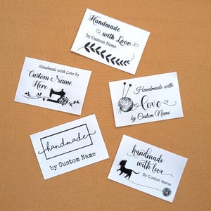 Peut inclure: Plusieurs étiquettes rectangulaires blanches avec du texte et des illustrations noirs. Les étiquettes indiquent "Handmade with Love" et "handmade", avec de l'espace pour un nom personnalisé. Les motifs incluent une machine à coudre, de la laine et un chat.