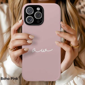 K&ouml;nnte beinhalten: Eine Boho Pink Handyh&uuml;lle mit wei&szlig;em "aw"-Schriftzug. Die H&uuml;lle hat eine einfarbige, ged&auml;mpfte rosa Farbe und einen Kameraausschnitt. Die Handyh&uuml;lle wird von einer Person gehalten.