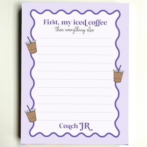 May include: A light purple notepad with a wavy dark purple border, featuring horizontal lines for writing. The text reads First, my iced coffee then everything else and Coach JR. Small illustrations of iced coffee cups are placed along the border.