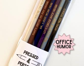 May include: A set of six wooden pencils in a clear plastic sleeve, each featuring a pink eraser and gold-stamped text including phrases like YOU'RE ON MUTE, THAT'S ABOVE MY PAY GRADE, IDK, I JUST WORK HERE, LET'S CIRCLE BACK NEVER, and NOPE, NOT TODAY!