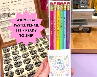 May include: A set of six pastel-colored pencils in a clear plastic sleeve. Each pencil is a different color, with text that reads "Stay W-Msical", "Powered by Pixie Dust", "Tea & Tiaras", and "Dream, Glow, Repeat". The packaging says "Add a little sparkle to your scribbles".