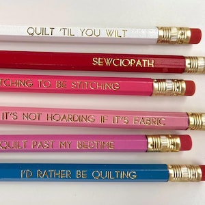 May include: A set of six wooden pencils in white, red, hot pink, light pink, magenta, and blue. Each pencil features a gold-colored metal ferrule, a pink eraser, and gold foil text: QUILT 'TIL YOU WILT, SEWCIOPATH, ITCHING TO BE STITCHING, IT'S NOT HOARDING IF IT'S FABRIC, I QUILT PAST MY BEDTIME, and I'D RATHER BE QUILTING.