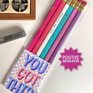 May include: A set of six pencils in a clear plastic sleeve, featuring colors of pink, white, teal, and purple. Each pencil is printed with motivational text including YOU GOT THIS, TRY YOUR BEST, YOU ARE AMAZING, BE KIND, MAKE GOOD CHOICES, and YOU ARE LOVED.