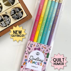 May include: A set of five hexagonal pencils in pink, yellow, green, light blue, and purple, each with a gold metal ferrule and eraser. The pencils feature gold foil text: DON'T WORRY, IT'LL QUILT OUT, MEASURE TWICE, CUT ONCE, MAKE QUILTING TAX-DEDUCTIBLE, PUT YOUR FOOT DOWN & QUILT, BOBBIN CHICKEN WINNER, and QUILT WHILE YOU'RE AHEAD.