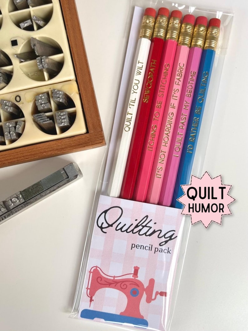 May include: A set of six pencils in a clear plastic sleeve, each featuring a different color and a unique quilting-themed phrase in gold lettering. The packaging includes a pink and white checkered label with a sewing machine illustration and the text Quilting pencil pack and Quilt Humor.