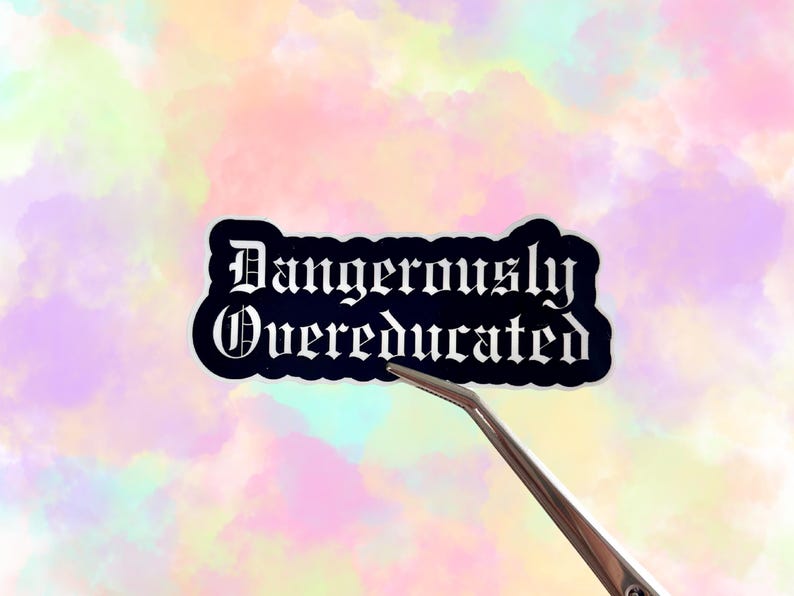 May include: A black sticker with the words "Dangerously Overeducated" in white gothic font. The sticker is held by a silver tweezer against a pastel watercolor background of pink, yellow, and blue.