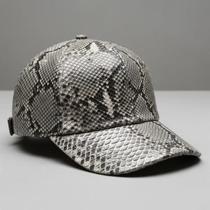 May include: A baseball cap featuring a snakeskin design in grey and white tones. The cap has a curved peak and an adjustable strap. The material has a textured finish.