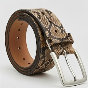 May include: A snakeskin-patterned belt with a silver-colored buckle. The belt is brown and tan with a dark brown border and a light brown interior. The buckle is rectangular and has a shiny finish.