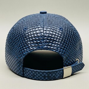 Peut inclure: Casquette de baseball bleue marine avec un motif textur&eacute; en forme d'&eacute;cailles. La casquette a une visi&egrave;re incurv&eacute;e, un bouton sur le dessus et une sangle r&eacute;glable avec une boucle en m&eacute;tal argent&eacute;. Accessoire de mode haut de gamme.
