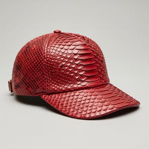 Può includere: Un cappellino da baseball rosso con un motivo strutturato e squamoso. Il cappellino presenta una visiera curva e un cinturino regolabile. Il materiale sembra essere pelle o simile, con una finitura lucida. Il cappellino è di colore rosso acceso.
