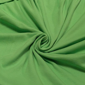 May include: Close-up of a vibrant green fabric, possibly knit or jersey, with soft folds and a subtle sheen. The fabric is tightly swirled in the center, creating a spiral effect. The color is a bright, cheerful green.