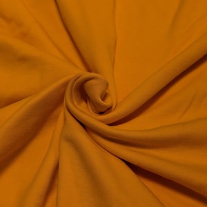 May include: Close-up of a folded piece of fabric in a warm, golden-yellow color. The fabric has a soft texture and is arranged in gentle folds and curves, creating a sense of depth and movement. The lighting highlights the fabric's texture.
