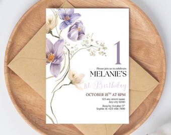 May include: A floral-themed birthday invitation with the text "MELANIE'S 1st Birthday" and event details. The invitation features watercolor illustrations of purple and cream-colored flowers. The invitation is placed on a wooden tray with a brown envelope.