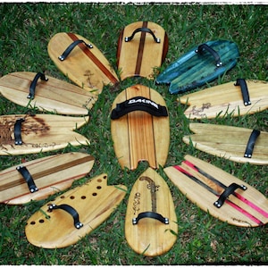 May include: A collection of 10 wooden surfboards with various designs and text, including "Old Soul", "The One", and "Dakine". The surfboards are arranged in a circle on a green grassy surface.