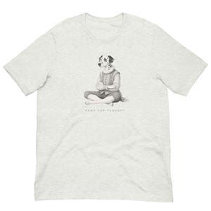 以下が含まれることがあります： 薄いグレーのTシャツ。白黒のイラストは、歴史的な衣装を着たダルメシアン犬が座っている様子を描いています。「PAWS FOR THOUGHT」の文字が下に印刷されています。Tシャツは半袖です。
