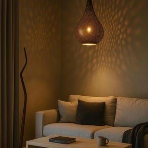 Puede incluir: Una lámpara colgante en forma de lágrima, de color bronce, cuelga sobre un sofá claro. La luz proyecta un diseño en la pared. Una mesa de centro de madera y una lámpara de pie también son visibles en la habitación.