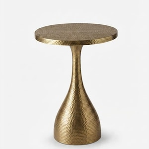 Op de afbeelding: Een ronde bijzettafel met een metalen messing afwerking en een opvallende gehamerde textuur over het gehele oppervlak. De tafel heeft een plat rond blad dat wordt ondersteund door een enkele, taps toelopende voet die naar onderen uitloopt.