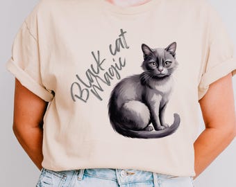 May include: A beige t-shirt featuring a gray illustration of a cat with the text "Black cat Magic". The cat is sitting with its tail curled. The shirt is made of a soft material.