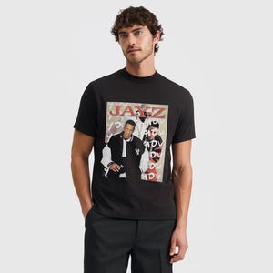 May include: Black t-shirt with a graphic featuring two people and the word "JAY-Z" in red and white. The image on the shirt has a camouflage background. The person in the image is wearing black trousers.