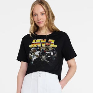 May include: Black t-shirt with a graphic of Jay-Z and the text "JAY-Z" in yellow and orange. The image on the shirt shows multiple images of Jay-Z. The t-shirt is worn by a person.
