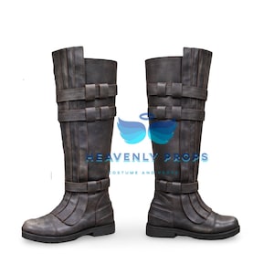 Puede incluir: Un par de botas de color marrón oscuro hasta la rodilla con textura desgastada, tres correas horizontales con hebillas en la caña y paneles cosidos verticales. El texto HEAVENLY PROPS COSTUME AND PROPS es visible entre las dos botas.