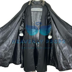 May include: A black costume with a long coat and cape. The costume has a high collar and a chest piece with vertical panels. The cape is lined with a shiny black fabric. The costume is displayed on a mannequin.