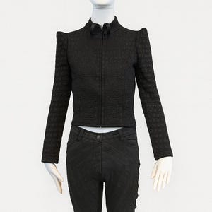 May include: A black long-sleeved jacket with a textured crocodile-skin pattern, a high collar, and a front zipper, paired with black trousers featuring subtle diagonal stitched lines and a button closure at the waist.