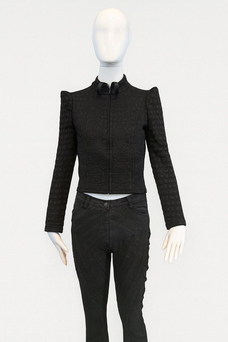 May include: A black long-sleeved jacket with a textured crocodile-skin pattern, a high collar, and a front zipper, paired with black trousers featuring subtle diagonal stitched lines and a button closure at the waist.