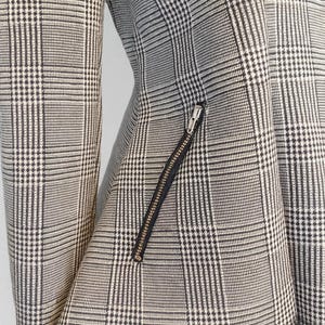 May include: A close-up of a black and white plaid blazer. The jacket features a diagonal zipper pocket and a black lining. The fabric has a classic glen plaid pattern.