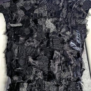 Puede incluir: Una prenda sin mangas confeccionada con un mosaico de diversos retazos de tela negra, incluyendo sat&eacute;n, malla transparente y piezas texturizadas de color plata met&aacute;lico brillante, superpuestas y cosidas para crear una superficie densa.