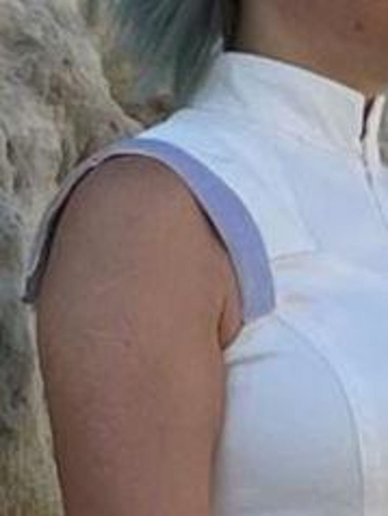 May include: A white sleeveless top featuring a high collar and a light purple trim along the shoulder seam. The garment is constructed with structured panels and a clean, fitted silhouette that sits close to the upper torso and shoulder area.
