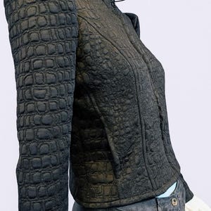 May include: A black jacket with a textured, embossed crocodile-skin pattern, featuring a high collar, structured shoulders, and long sleeves. The jacket is worn over dark gray pants with a visible button closure at the waistline.