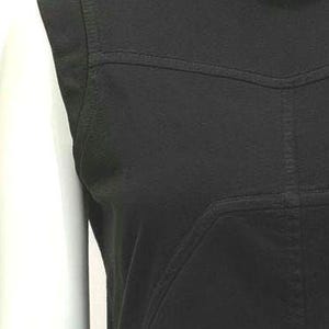 May include: Close-up of a black sleeveless top. The top features stitched detailing across the shoulders and chest. The fabric appears to be a matte material. The neckline is rounded.