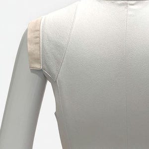May include: A sleeveless white top featuring a high collar and a structured shoulder design with contrasting beige fabric panels. The garment is fitted, showcasing vertical seam detailing along the torso and a clean, minimalist construction.