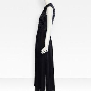 Puede incluir: Un vestido negro sin mangas hasta el suelo con un corpi&ntilde;o de encaje floral y una capa superpuesta transparente. La falda est&aacute; hecha de tela negra s&oacute;lida con una abertura lateral, exhibido sobre un maniqu&iacute; de color blanco.