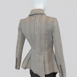 May include: A gray and white plaid blazer with a peplum waist, displayed on a mannequin. The blazer has a notched collar, long sleeves with zippered cuffs, and a tailored fit. The mannequin is wearing black pants.