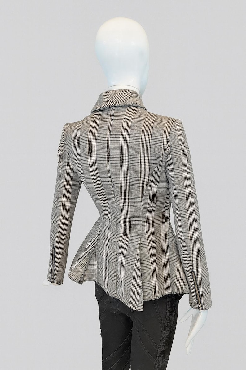 May include: A gray and white plaid blazer with a peplum waist, displayed on a mannequin. The blazer has a notched collar, long sleeves with zippered cuffs, and a tailored fit. The mannequin is wearing black pants.