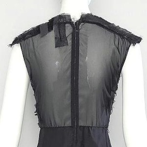 Puede incluir: Una blusa negra sin mangas con un cuerpo semitransparente y una cremallera vertical central. La prenda presenta bordes deshilachados tipo encaje a lo largo de los hombros y las sisas, creando una apariencia de capas.