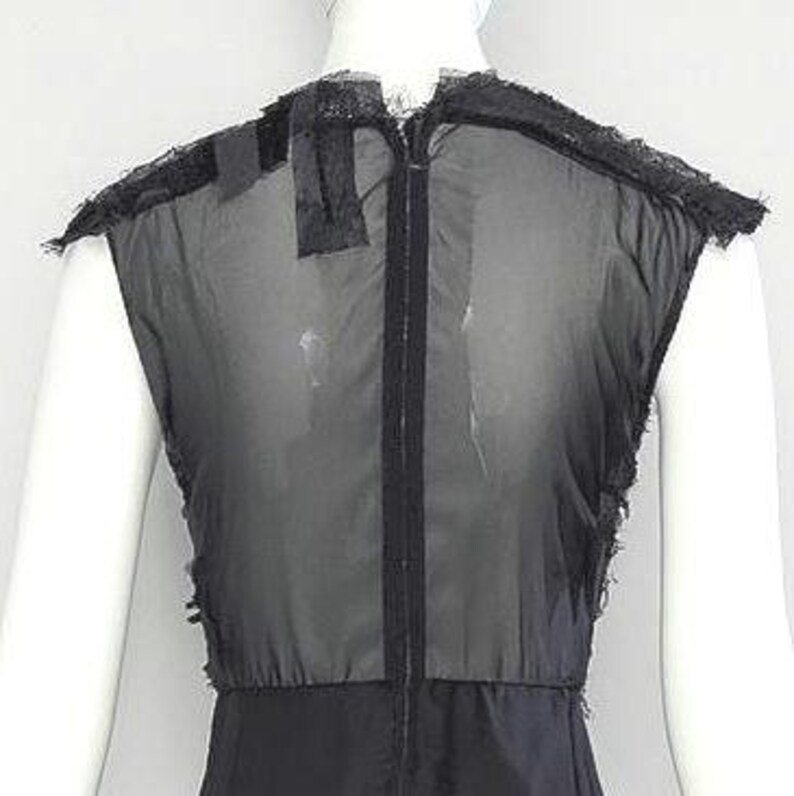 Puede incluir: Una blusa negra sin mangas con un cuerpo semitransparente y una cremallera vertical central. La prenda presenta bordes deshilachados tipo encaje a lo largo de los hombros y las sisas, creando una apariencia de capas.