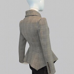May include: A gray and white plaid blazer with a peplum hem and a notched collar. The jacket has long sleeves with a zipper detail on the cuff. The blazer is displayed on a mannequin.