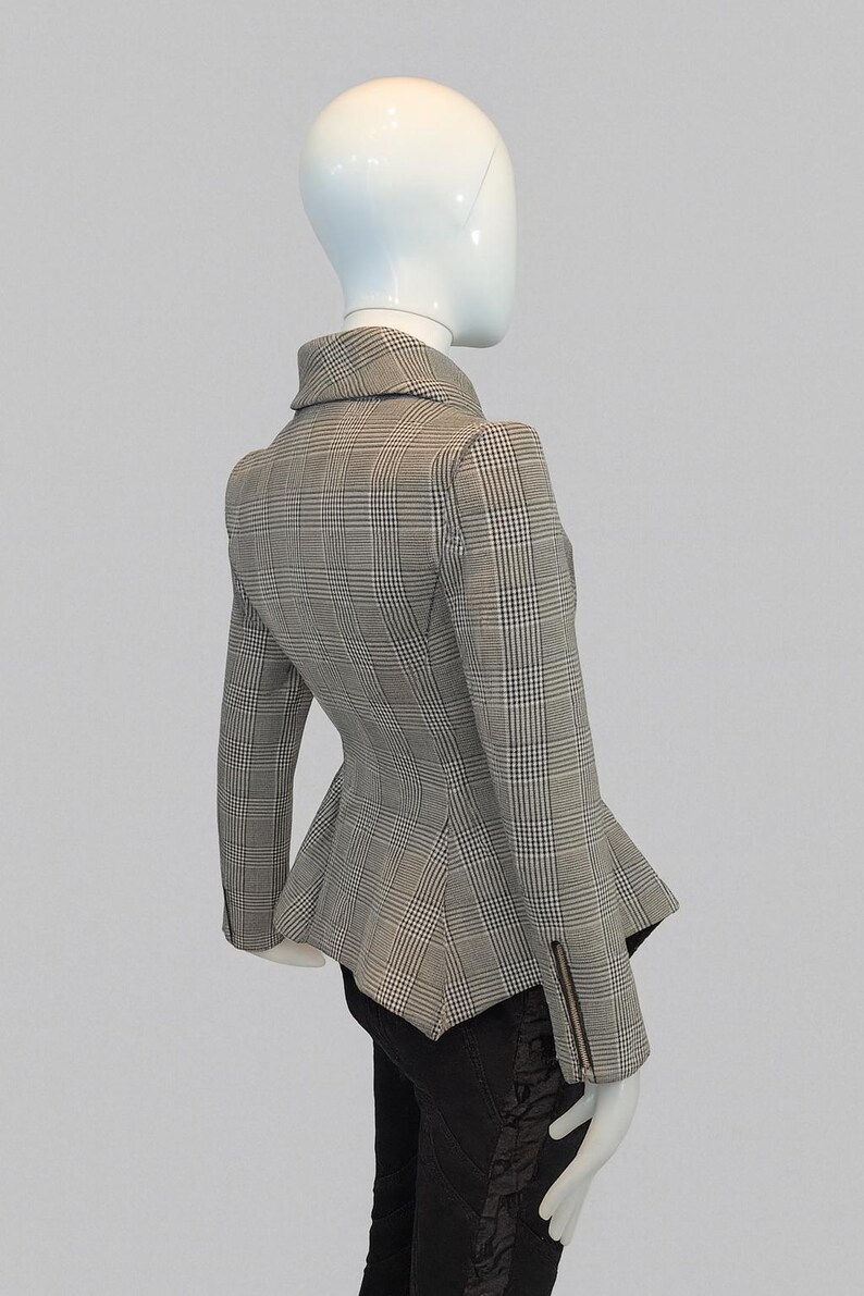 May include: A gray and white plaid blazer with a peplum hem and a notched collar. The jacket has long sleeves with a zipper detail on the cuff. The blazer is displayed on a mannequin.