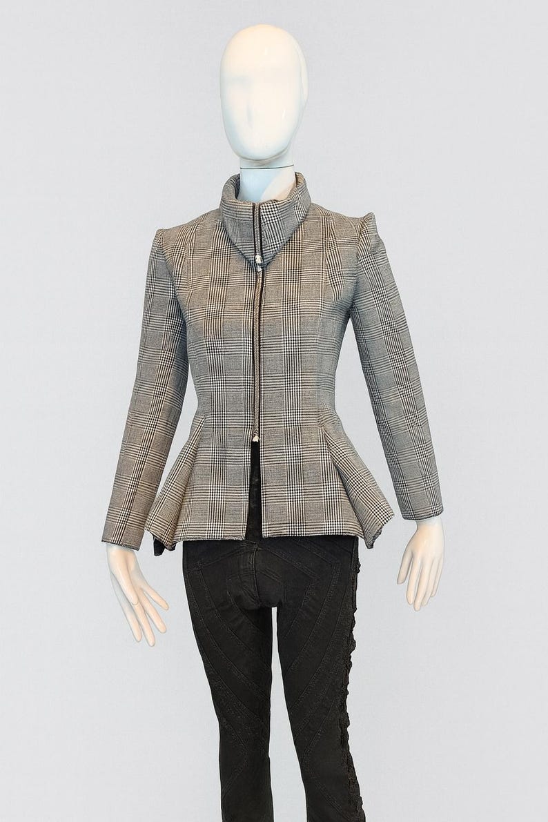 May include: A gray and white plaid jacket with a high collar and a peplum waist. The jacket has long sleeves and a black zipper down the front. The mannequin is also wearing black pants.