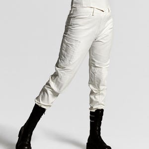 May include: Off-white cargo pants featuring a high-waisted fit, side utility pockets, and reinforced knee panels, paired with a sleeveless white top and black mid-calf boots with a thick sole and buckle detailing.