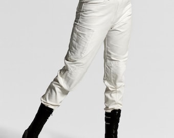 May include: Off-white cargo pants featuring a high-waisted fit, side utility pockets, and reinforced knee panels, paired with a sleeveless white top and black mid-calf boots with a thick sole and buckle detailing.