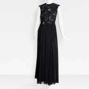 May include: A floor-length black sleeveless dress featuring a bodice adorned with layered fabric floral appliqués and a sheer overlay. The skirt is made of a solid black fabric that falls to the floor, creating a long, flowing silhouette.