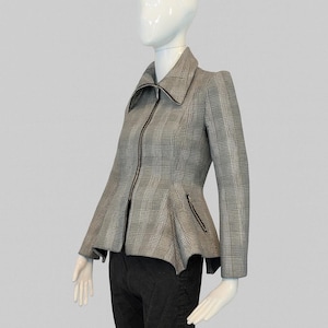 May include: A grey and black checked jacket with a peplum waist and a zip-up front. The jacket features a wide collar and small pockets. The jacket is displayed on a mannequin with black trousers.