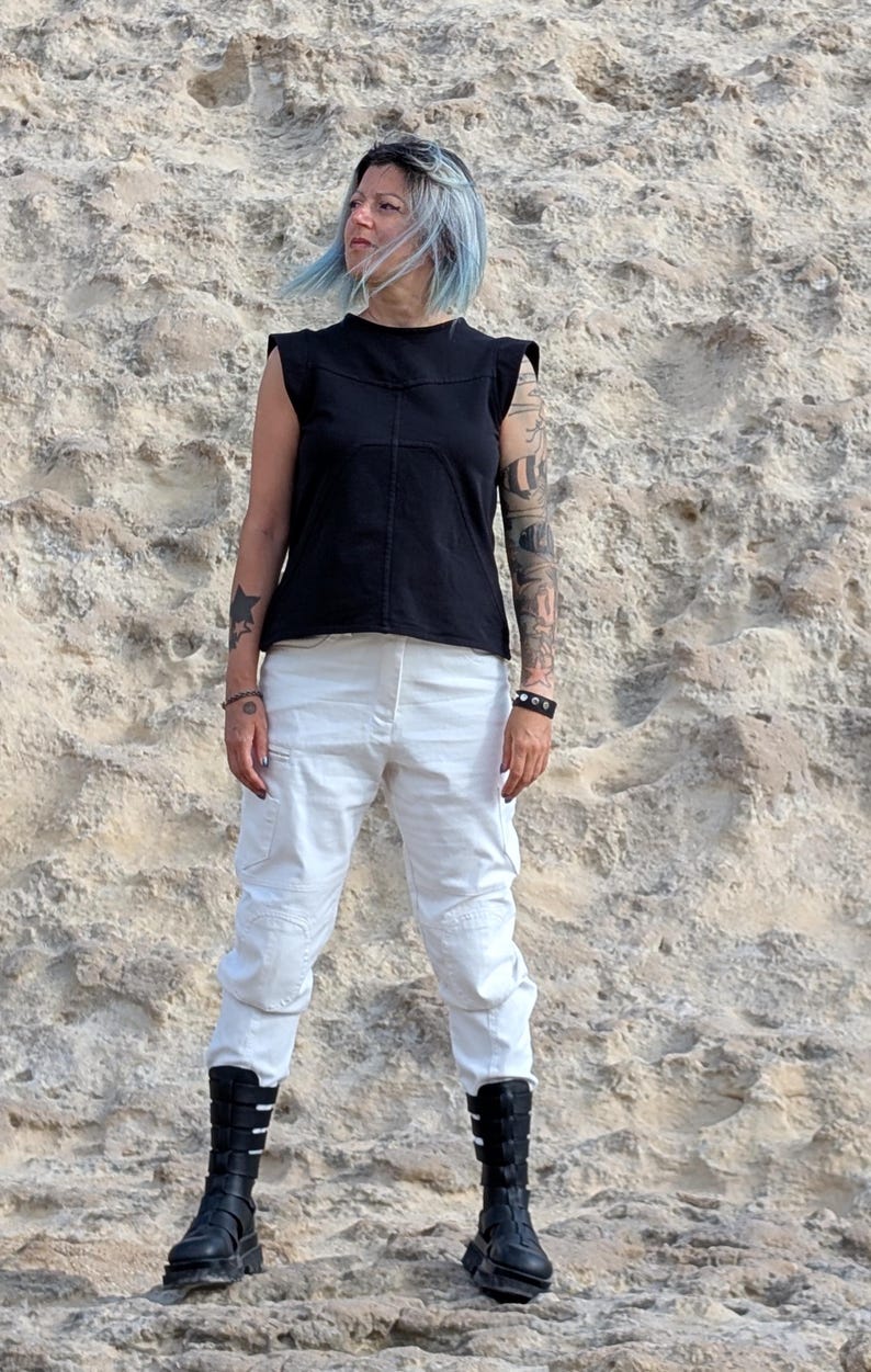 May include: A black sleeveless top with structured shoulders and visible seam detailing paired with white cargo-style pants and black mid-calf boots featuring multiple horizontal straps and buckles on the front.