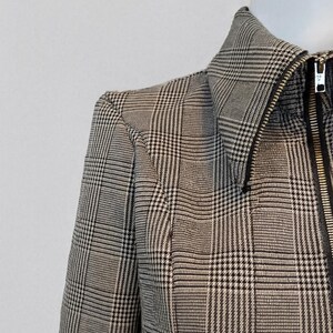 May include: Close-up of a black and white plaid jacket with a zipper closure. The jacket is displayed on a mannequin. The fabric has a classic houndstooth pattern.